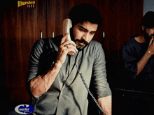 a man talking on a phone in front of a sign that says ' khurshid films '