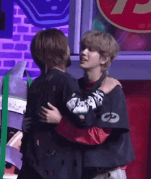 two men are hugging each other in front of a brick wall .