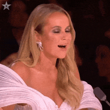 a woman in a white dress is sitting in front of a microphone with her mouth open ..