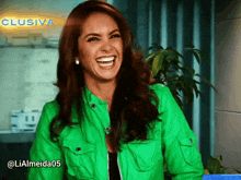 a woman in a green jacket is laughing in front of a sign that says clusiva