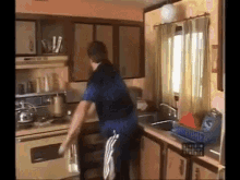 a man in a blue shirt is standing in a kitchen near a sink and oven