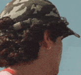 a close up of a person wearing a camouflage hat and earrings