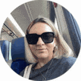 a woman wearing sunglasses is sitting in a blue chair on a train