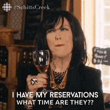 a woman is holding a glass of wine and says i have my reservations what time are they