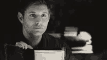 a black and white photo of a man holding a book in his hands .