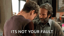 a man with a beard is standing next to another man with the words `` it 's not your fault '' on the screen .