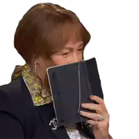 a woman covering her face with a book and a chanel brooch