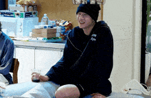 a man wearing a beanie is sitting on a couch holding a cup of coffee .