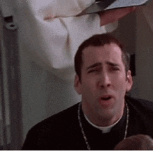 a priest is making a funny face while holding a bible in his hands .