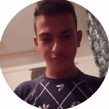 a young man wearing an adidas shirt looks at the camera with his eyes closed