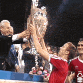 a man in a red shirt is holding a trophy with a forest logo on his shirt
