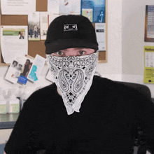 a man wearing a bandana and a black hat stands in front of a bulletin board with papers on it