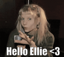 a girl with blonde hair says hello ellie < 3 in white letters