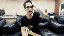 a man is sitting on a couch with a guitar in his hand .