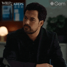 a man with a beard is sitting at a desk with the words what are you doing below him