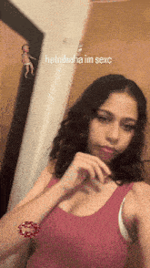 a girl in a pink tank top is taking a selfie with a baby in the background