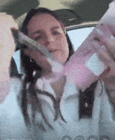 a woman in a car is holding a pink bottle in her hand