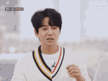 a man wearing a white sweater with a black yellow and red striped collar is talking in korean
