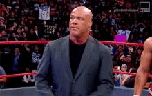 a bald man in a suit is standing in a wrestling ring with a crowd watching .