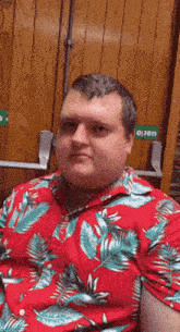 a man wearing a red hawaiian shirt is sitting in front of a wooden door that says open