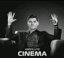 a man in a suit is sitting in a chair with his hands in the air and the words absolute cinema below him