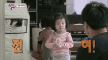 a little girl is standing next to a man in a living room and talking to him .