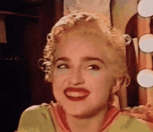 a woman with blonde hair and red lips is smiling in front of a mirror in a room .
