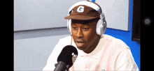 a man wearing headphones and a hat with the letter g on it talks into a microphone