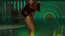 a woman in a bodysuit is dancing in front of a green light
