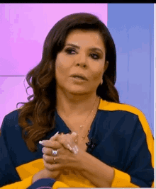 a woman wearing a blue and yellow shirt is sitting with her hands folded .
