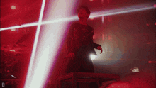 a man stands on a stage in front of a red light with the letter d on the bottom right
