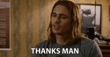 a man with long hair is wearing a gray shirt and says thanks man