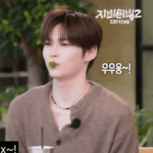 a young man with a green leaf in his mouth is sitting in front of a sign that says ' zotving ' on it