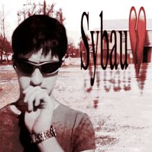 a man wearing sunglasses and a watch stands in front of sybau