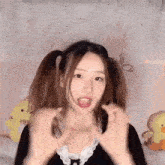 a girl with pigtails is making a funny face and making a heart shape with her hands .