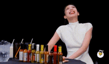 a woman is standing in front of a table full of bottles of hot sauce and laughing .