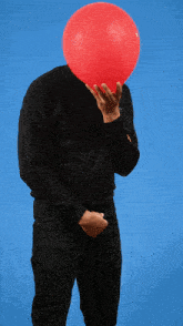 a man in a black sweatshirt holds a red balloon in front of his face