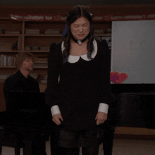 a woman in a black dress stands in front of a man playing a piano in front of a sign that says indicators door