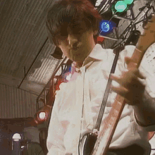 a man in a white shirt is playing a guitar in front of a bunch of lights