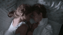 a man and a woman are laying on a bed holding hands and looking at each other .