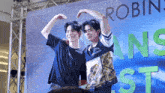 two men are making a heart shape with their hands in front of a sign that says robin