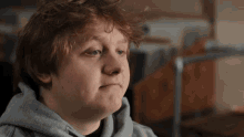 a young man with red hair wearing a grey hoodie looks at the camera