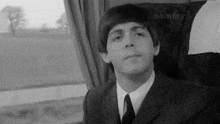 a black and white photo of a man in a suit and tie sitting in a train car .