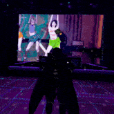 a man in a green shirt is standing in front of a large screen with a picture of three girls on it