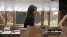 a woman is standing in a kitchen next to a window with a bag on the counter .