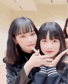 two young girls are posing for a picture together and making a heart with their hands .