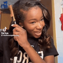 a girl is smiling while holding a hair straightener and a tiktok video is displayed