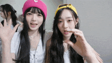 a girl wearing a pink hat with a heart on it is standing next to another girl wearing a yellow hat