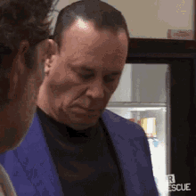a man in a blue suit and black shirt is standing next to another man in front of a refrigerator .