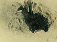 a person in a black jacket is laying on a sandy surface
